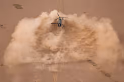 Chinook-transporthelikopter boven een enorme wolk opstuivend zand. Alleen maar bruin/oranjetinten.