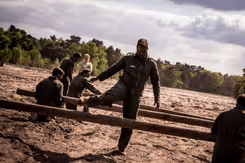 Militair stapt over houten balk op hindernisbaan.