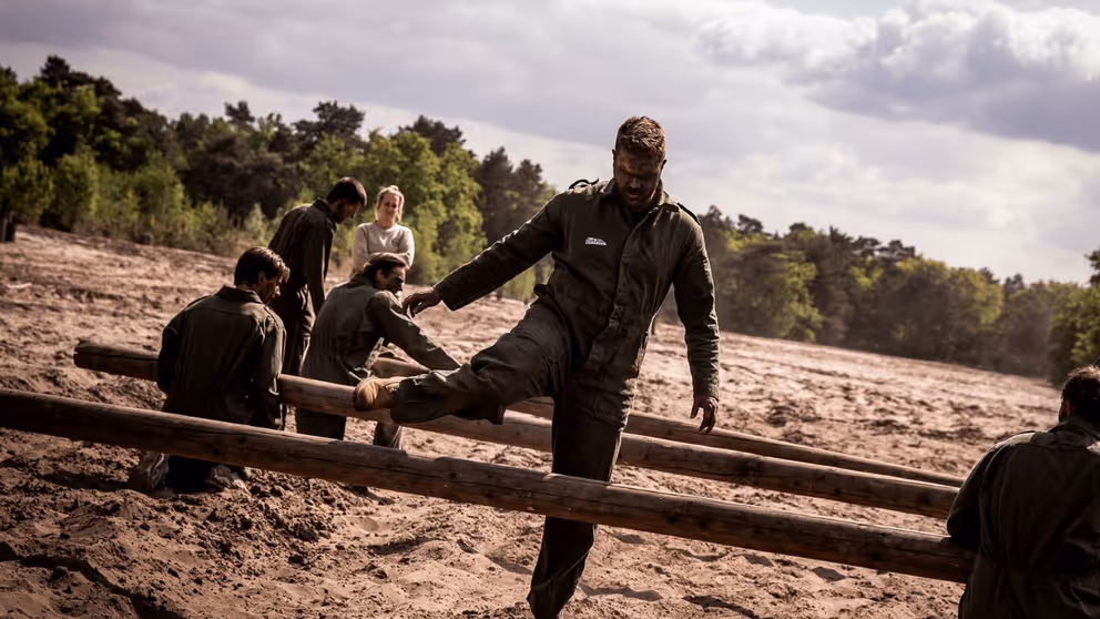 Militair stapt over houten balk op hindernisbaan.