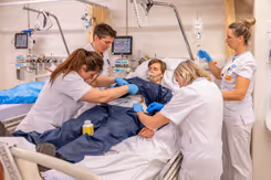 4 zorgmedewerkers behandelen een patiënt die in bed ligt tijdens een oefening.