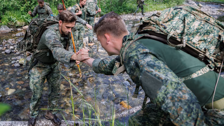 Een militair reikt zijn collega de hand en helpt hem een slootje oversteken.