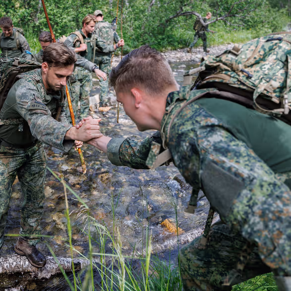 Een militair reikt zijn collega de hand en helpt hem een slootje oversteken.