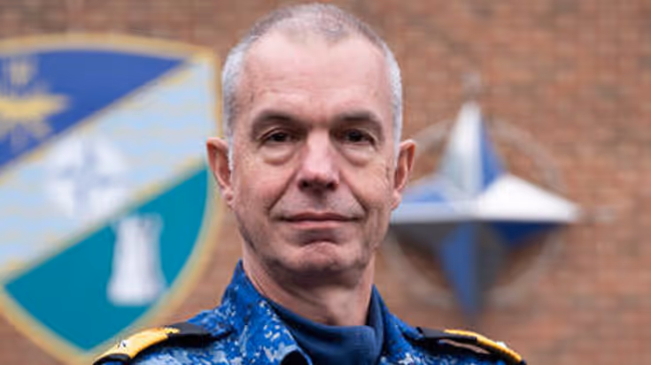 Portretfoto van commandeur Arjen Warnaar, met armen over elkaar in een blauw camouflage-uniform.