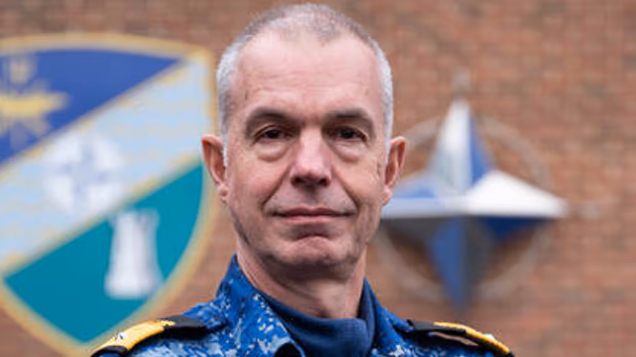 Portretfoto van commandeur Arjen Warnaar, met armen over elkaar in een blauw camouflage-uniform.