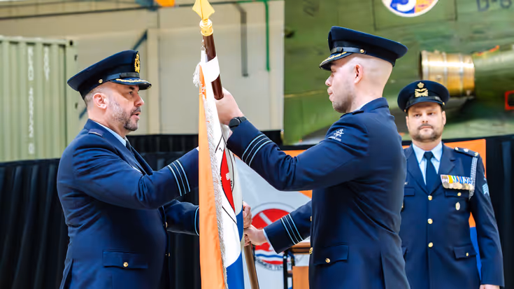 Majoor Jeroen van Asperen overhandigt aan majoor Lesley Dröge een vlag. Achter hen kijkt een militair toe.