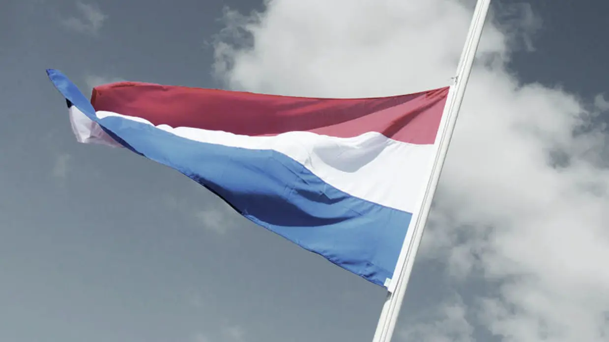 Nederlandse vlag halfstok tegen grijze wolkenlucht.