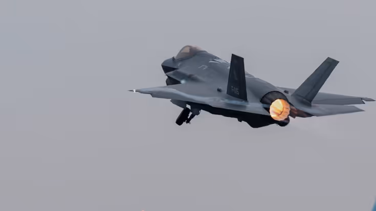 Een F-35 vliegt, terwijl daaronder reguliere vliegtuigen taxiën.