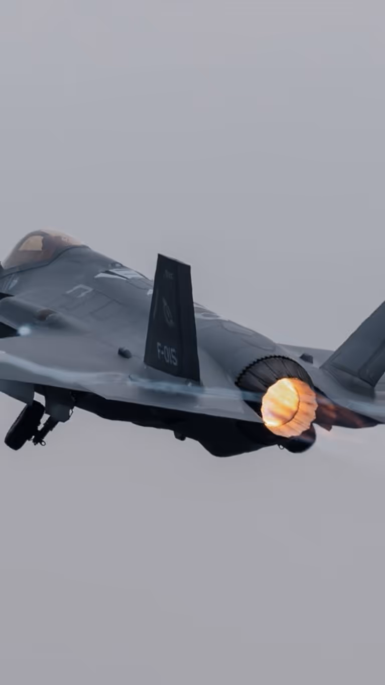 Een F-35 vliegt, terwijl daaronder reguliere vliegtuigen taxiën.