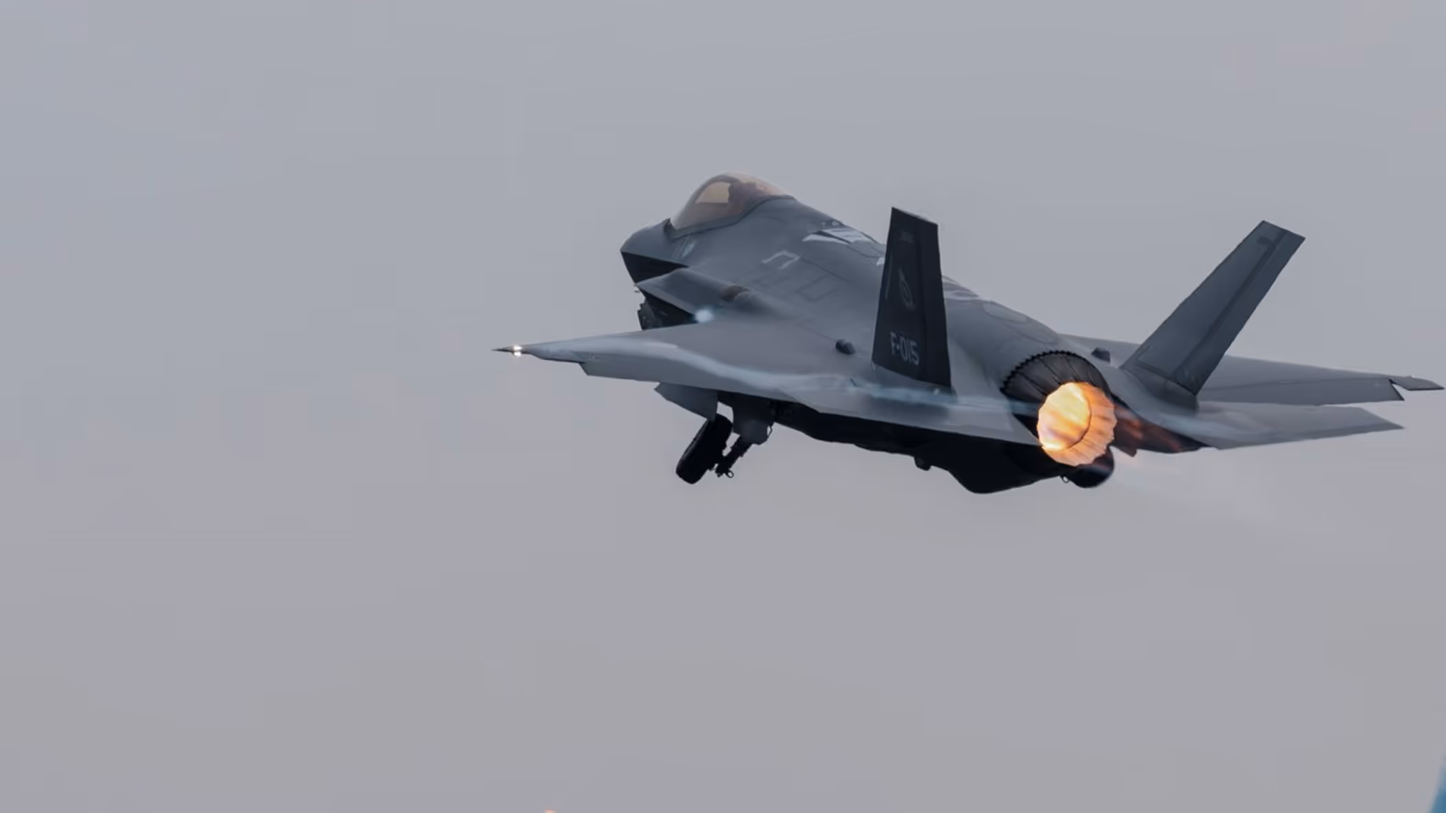 Een F-35 vliegt, terwijl daaronder reguliere vliegtuigen taxiën.