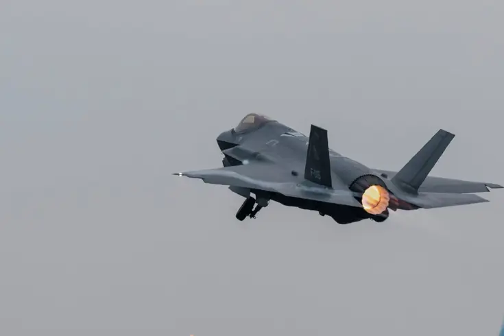 Een F-35 vliegt, terwijl daaronder reguliere vliegtuigen taxiën.