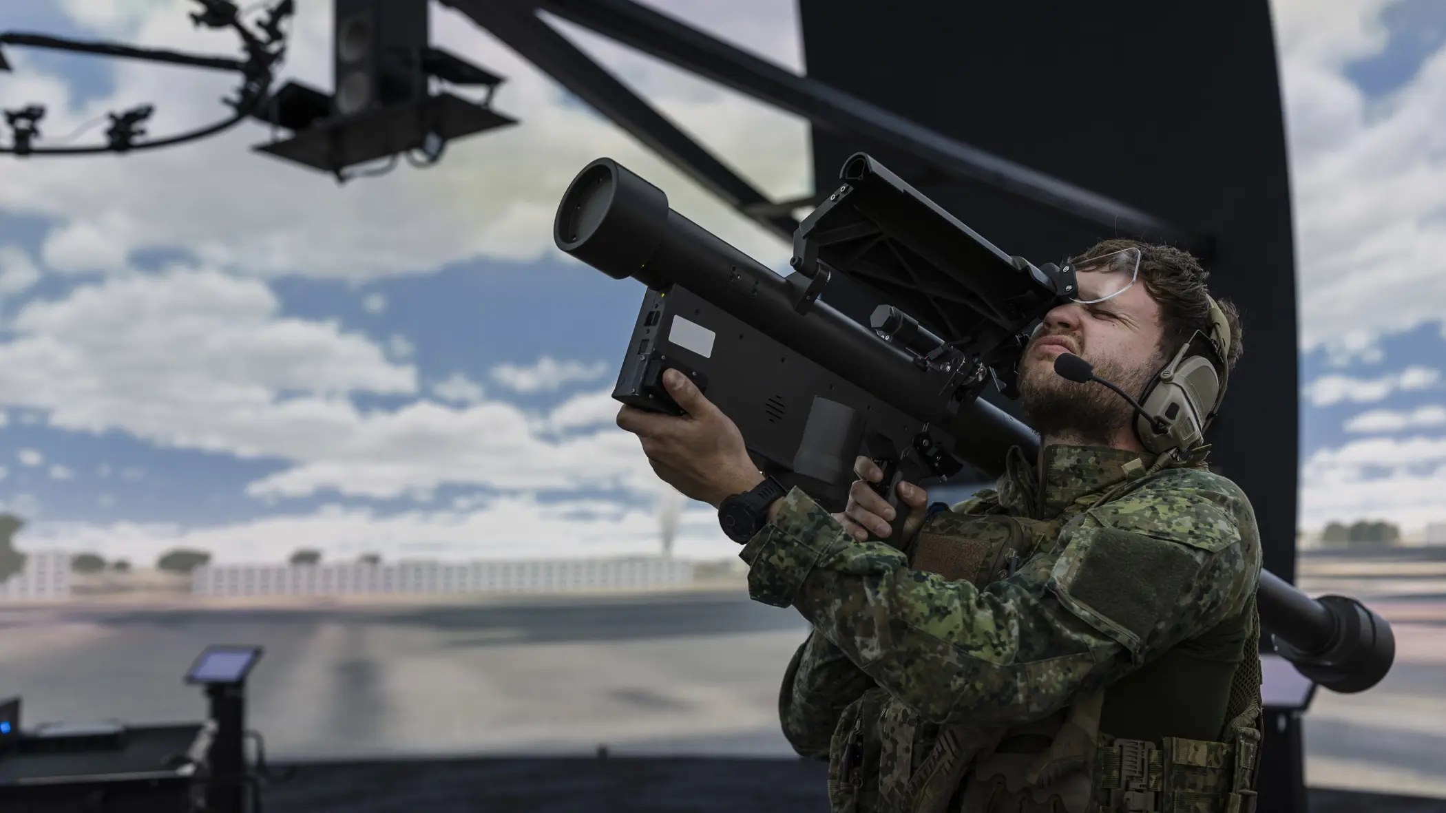 Een militair richt met een wapen op zijn schouder in de lucht. Daarbij knijpt hij een oog dicht. Hij bevindt zich in een ronde simulatieruimte.