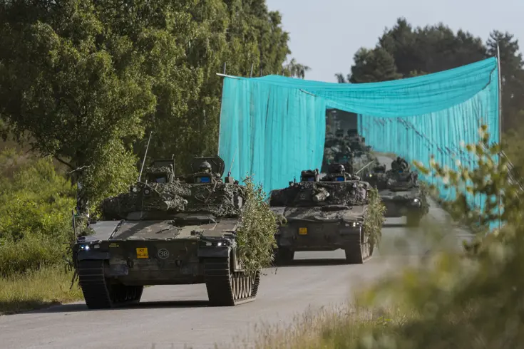 Militaire voertuigen rijden achter elkaar over de weg.