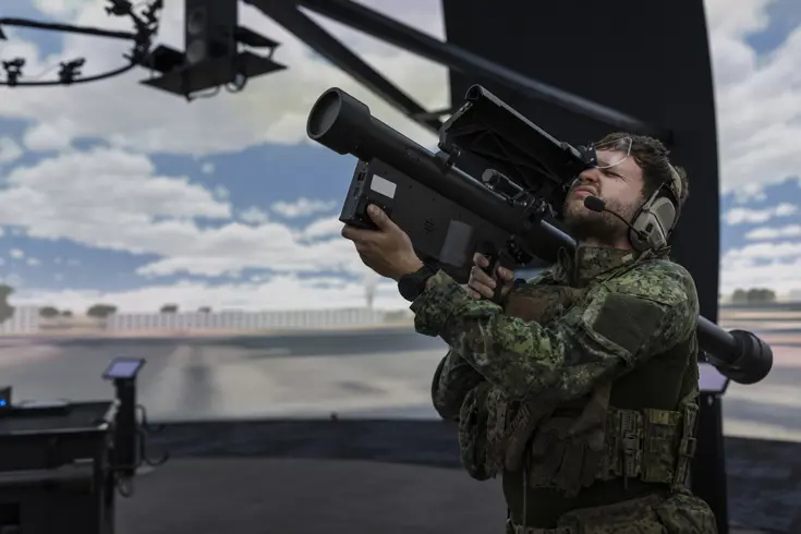 Een militair richt met een wapen op zijn schouder in de lucht. Daarbij knijpt hij een oog dicht. Hij bevindt zich in een ronde simulatieruimte.