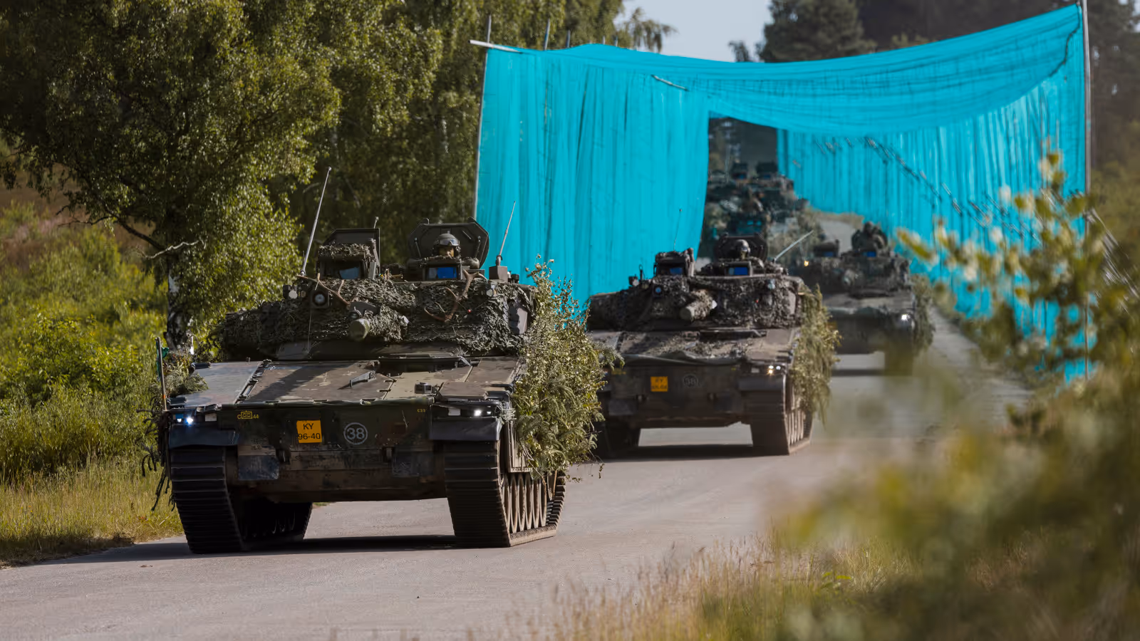 Militaire voertuigen rijden achter elkaar over de weg.
