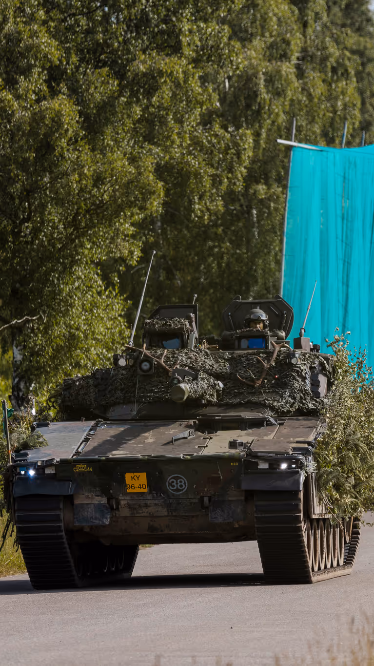Militaire voertuigen rijden achter elkaar over de weg.