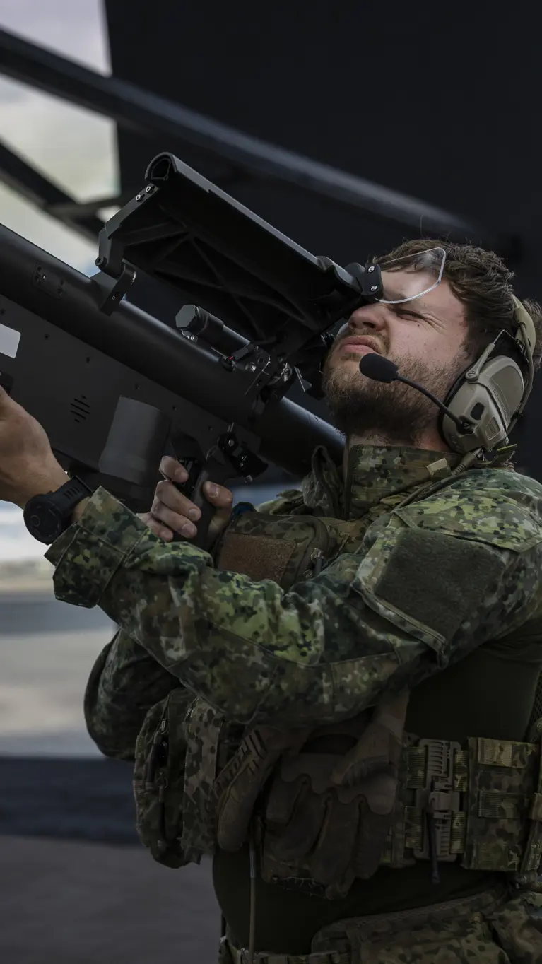 Een militair richt met een wapen op zijn schouder in de lucht. Daarbij knijpt hij een oog dicht. Hij bevindt zich in een ronde simulatieruimte.