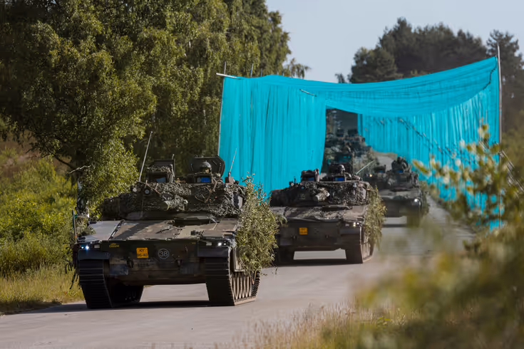 Militaire voertuigen rijden achter elkaar over de weg.