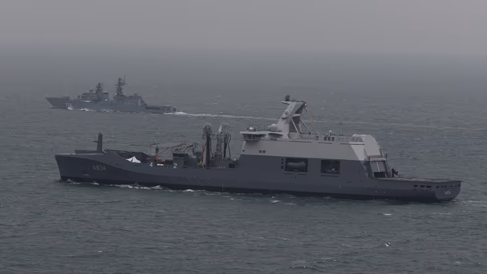 Een marineschip escorteert een ander schip op zee.