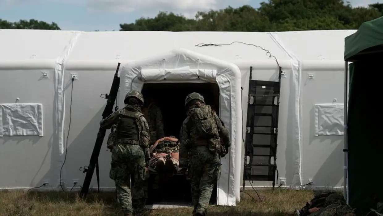 2 militairen dragen een brancard een witte unit in. 