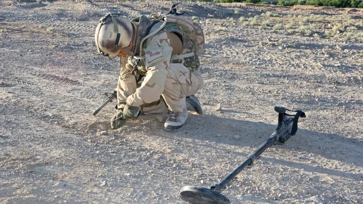 Militair zoekt tijdens een voetpatrouille in Uruzgan naar eventueel verstopte bermbommen.