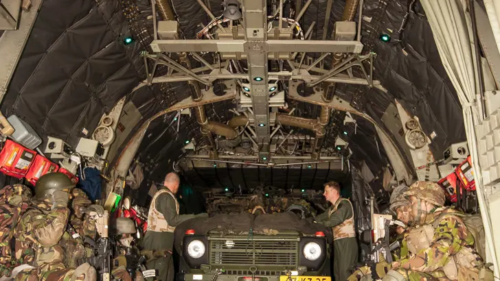 Een groep militairen met een militair voertuig in een C-130 Hercules-transportvliegtuig.