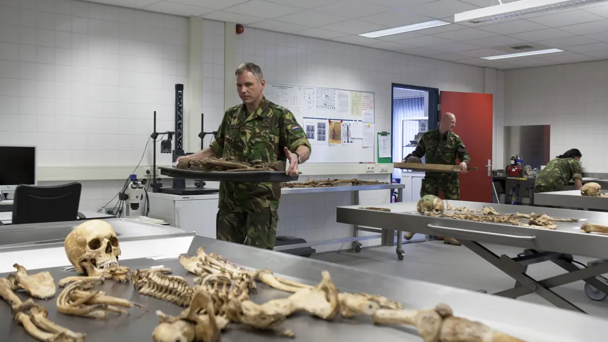 Medewerkers van de Bergings-en Identificatiedienst Koninklijke Landmacht dragen gevonden resten van onbekende soldaten het laboratorium in.