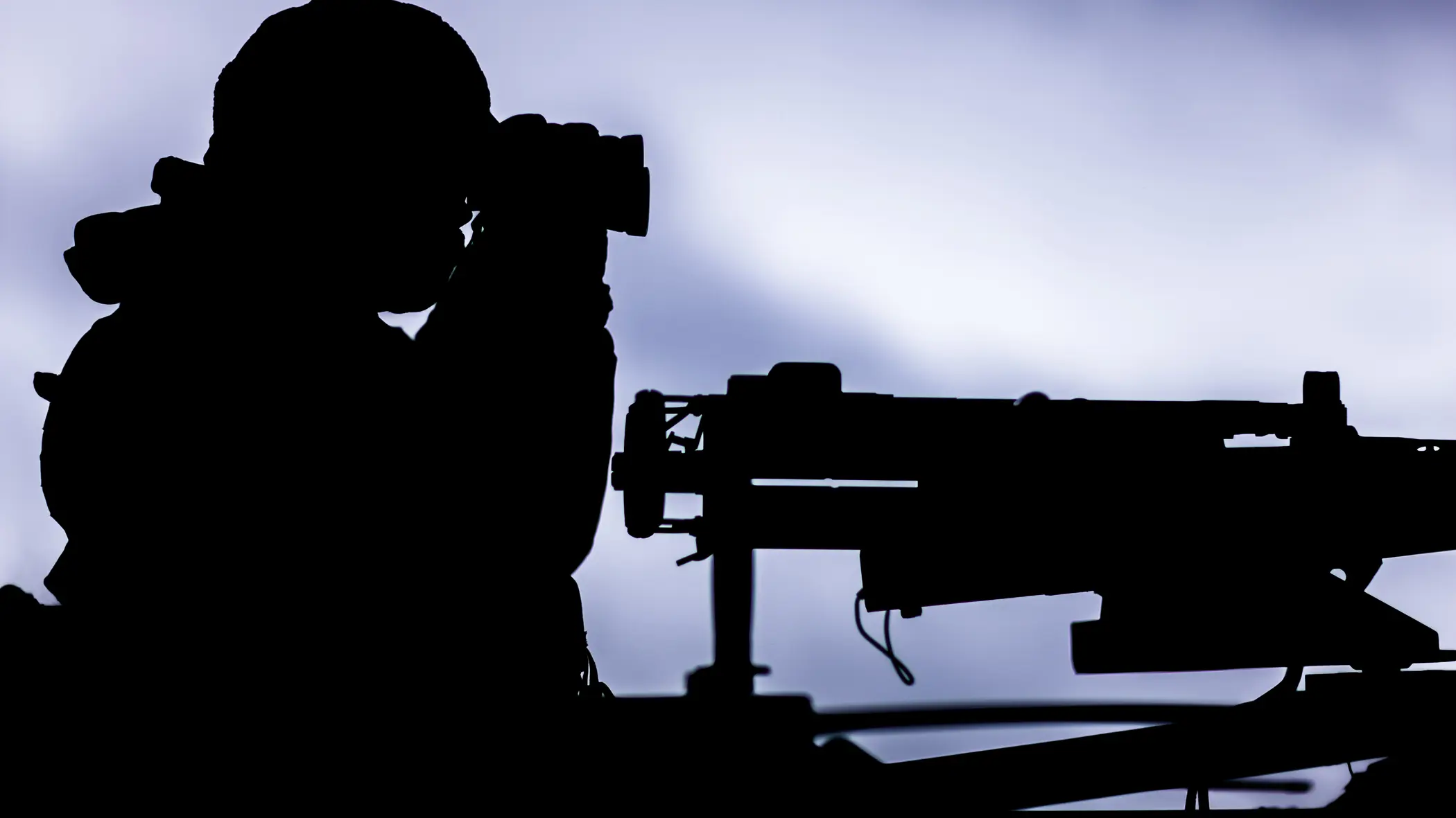 Het silhouet van een militair achter een mitrailleur. 