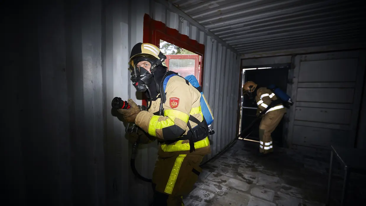 2 brandweerlieden lopen door een container op het brandweeroefencentrum.