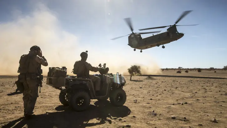 2 militairen kijken hoe een Chinook landt in een woestijn.