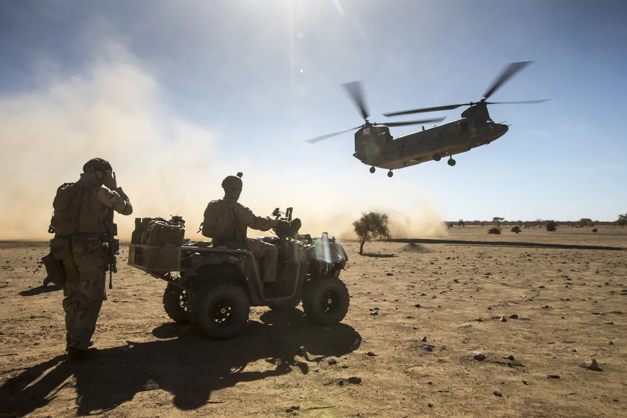 2 militairen kijken hoe een Chinook landt in een woestijn.