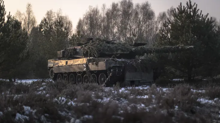 Een gecamoufleerde gevechtstank rijdt door besneeuwd terrein.