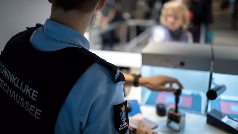 Een lid van de KMar gaat een paspoort stempelen.