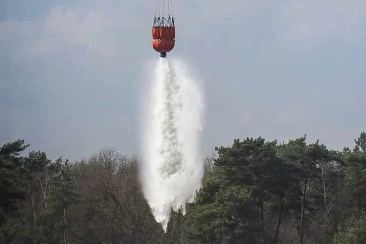 Een bambi bucket lost water boven een bos.