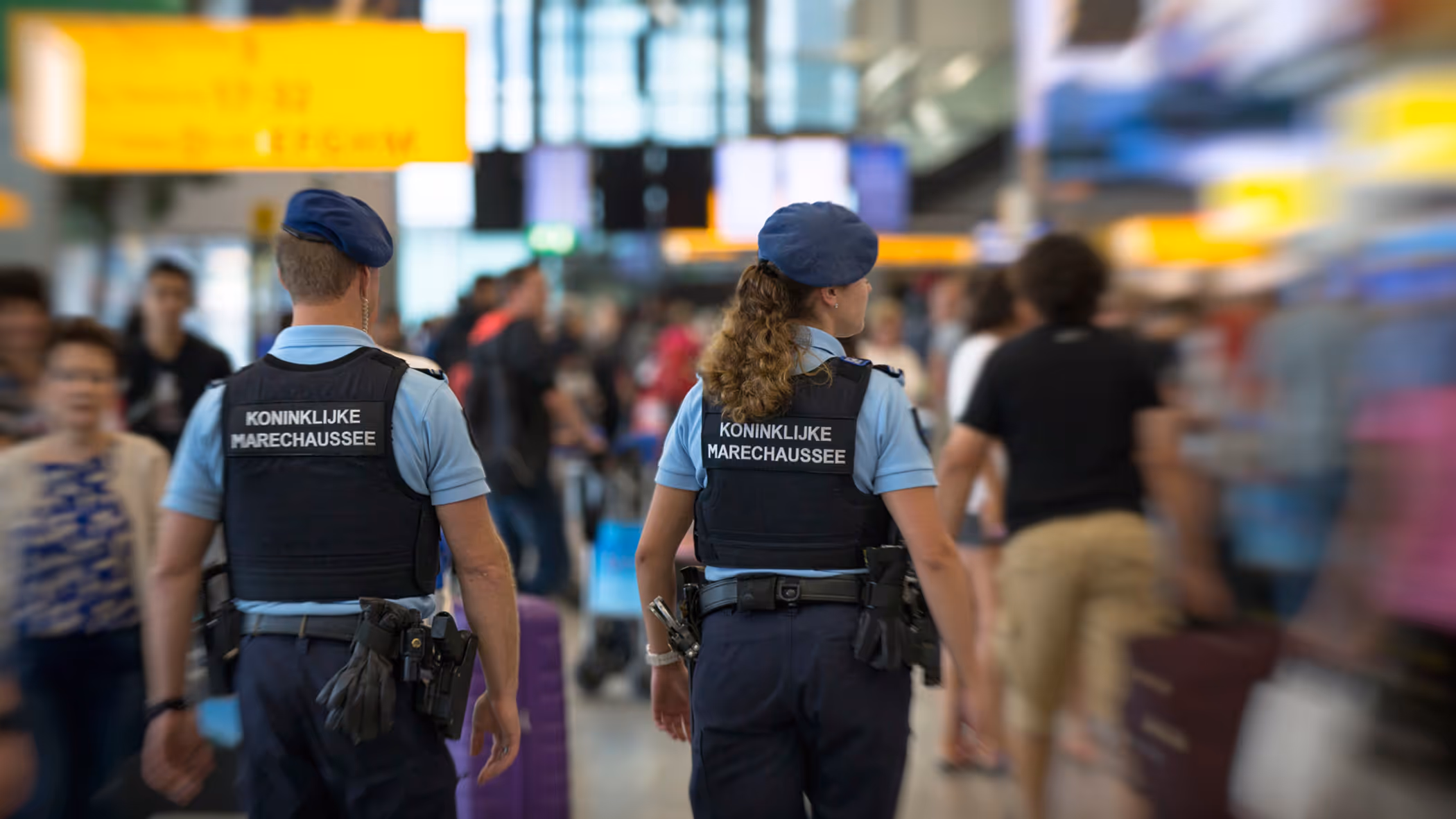 Twee marechaussees tussen het publiek op Schipol, op de rug gezien.