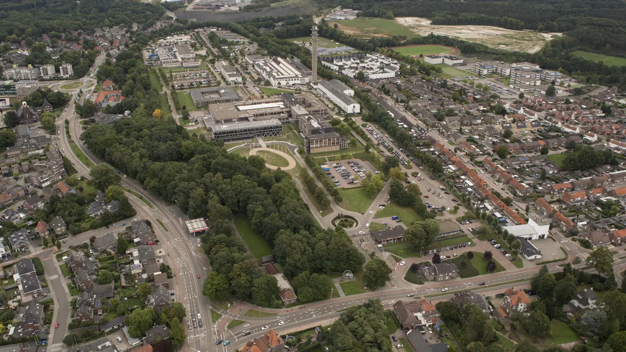 Luchtfoto van een gebouwencomplex, omzoomd met bomen en grenzend aan woonwijken.