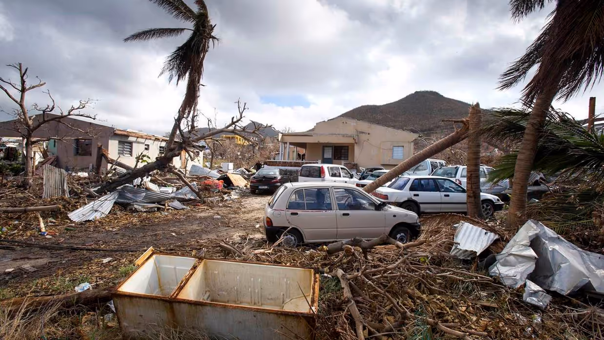 Een woonwijk na de verwoestende passage van orkaan Irma, met zwaar beschadigde huizen, auto’s en omgevallen palmbomen.