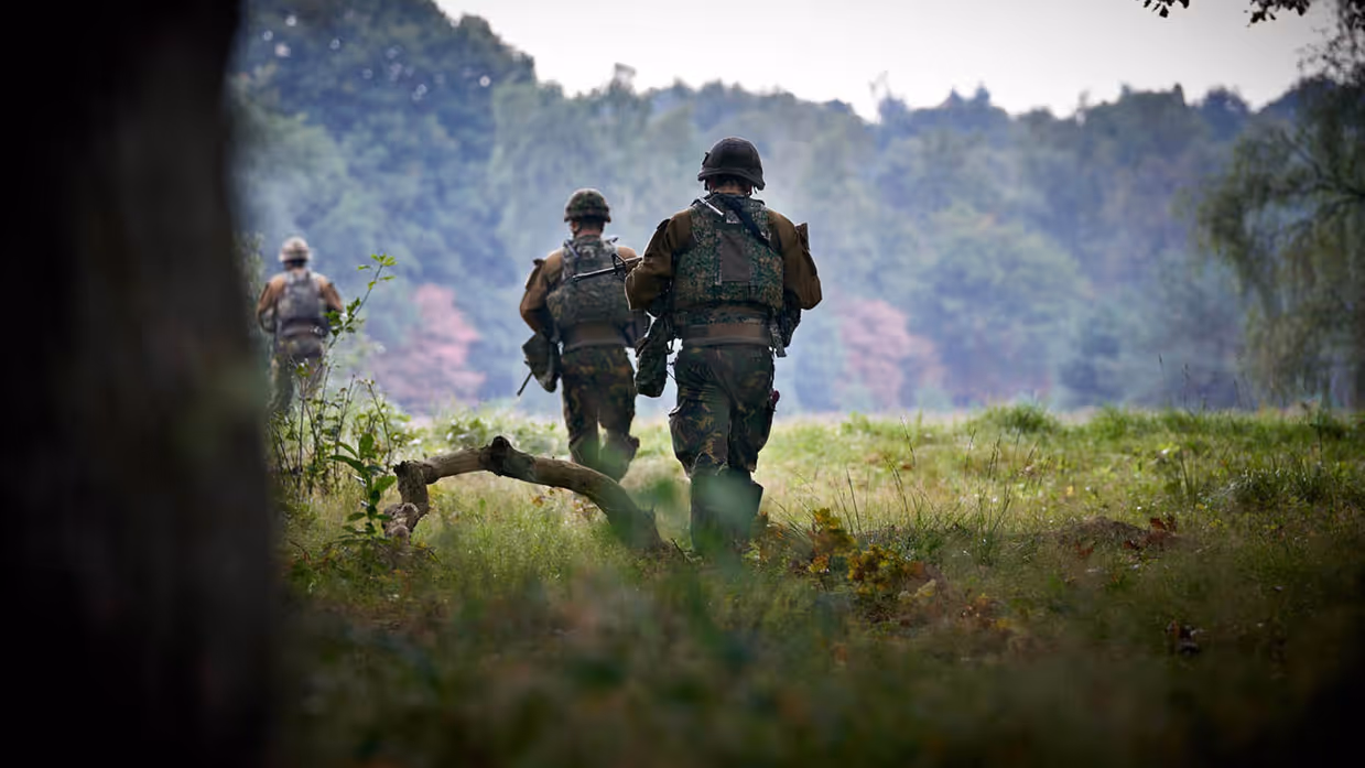 Militairen, vanaf de rug bezien, lopen door het beboste militaire oefenterrein De Vlasakkers.
