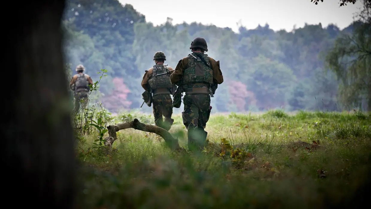 Militairen, vanaf de rug bezien, lopen door het beboste militaire oefenterrein De Vlasakkers.