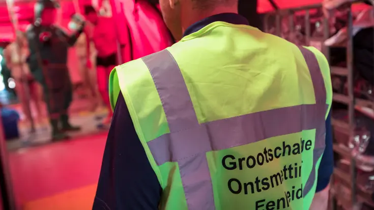 Man met geel hesje. Tekst op achterkant hesje: Grootschalige Ontsmettings Eenheid.