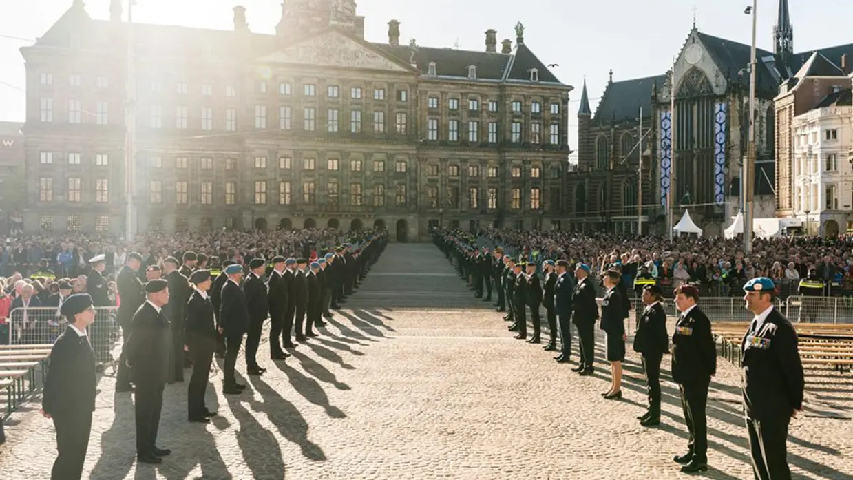 Militairen staan opgesteld op de Dam in Amsterdam, publiek erachter.