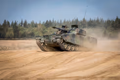 Een CV90 rijdt over een zandvlakte. 