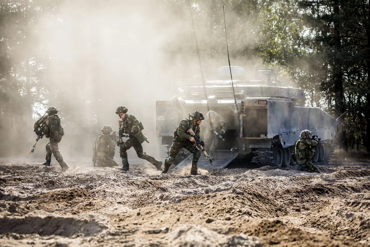 Een CV90 in het veld met om het voertuig heen een aantal net uitgestapte militairen.
