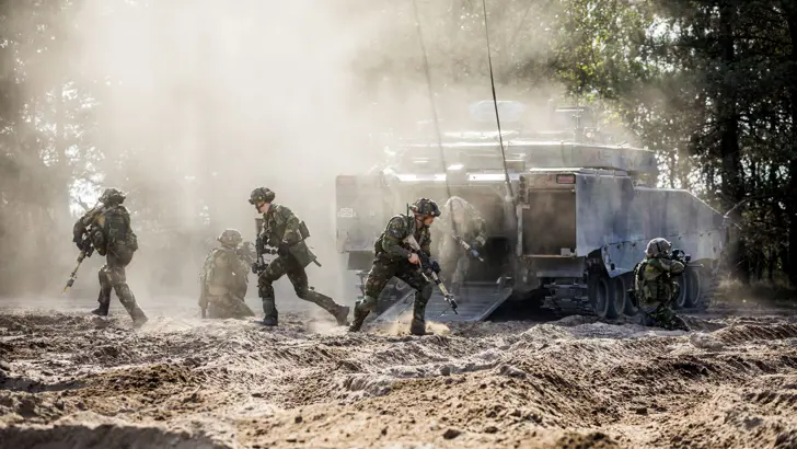 Een CV90 in het veld met om het voertuig heen een aantal net uitgestapte militairen.