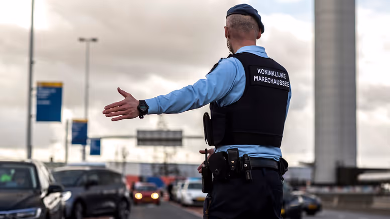 Een marechaussee op de rug gezien, wijst een voertuig naar de controleplaats.