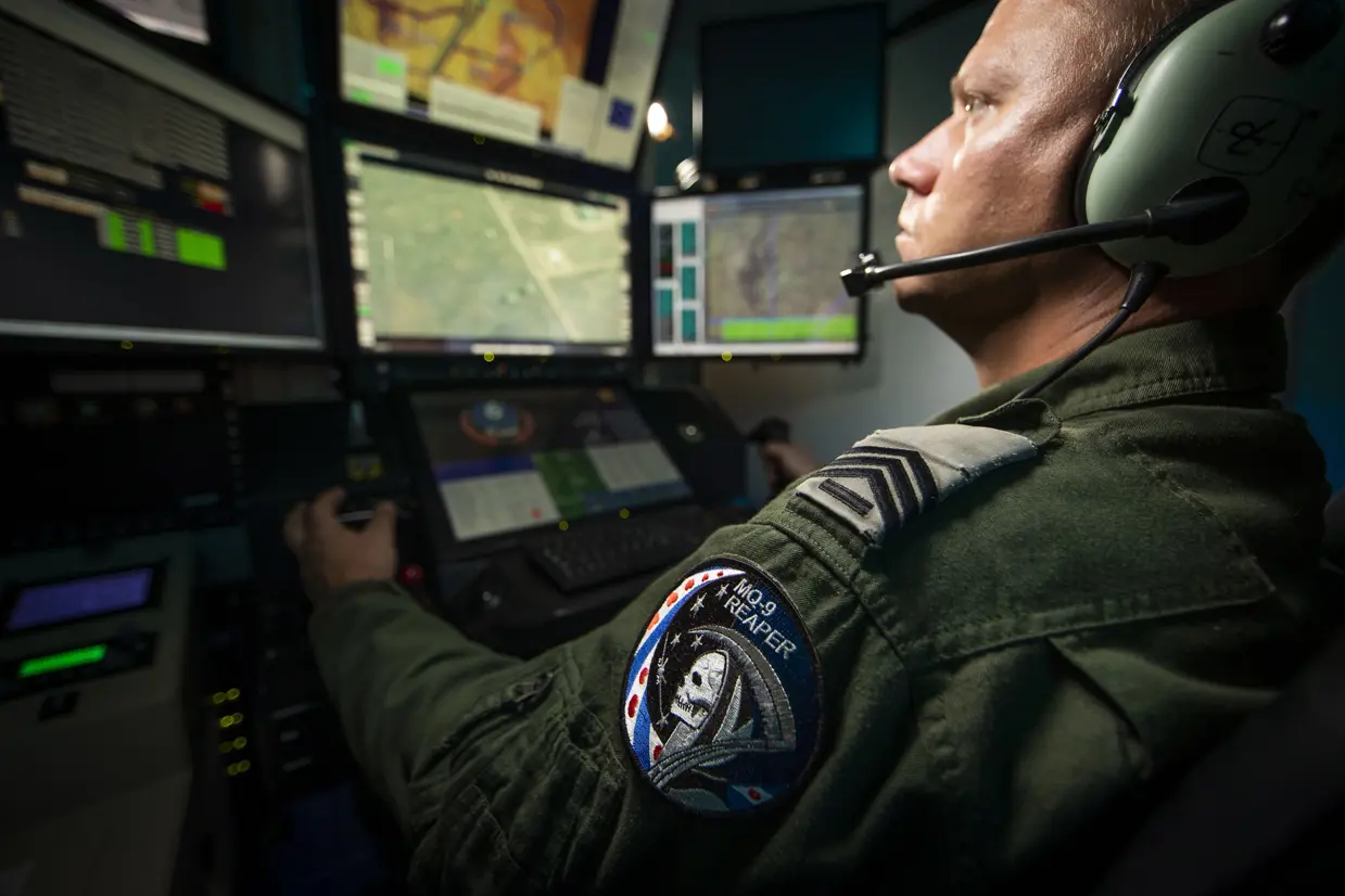 Een vlieger en sensoroperator vliegen een toestel vanachter beeldschermen. Op de mouw een MQ-9 Reaper-embleem met Magere Hein en de Friese vlag.