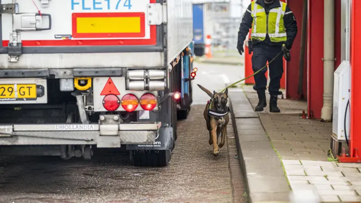 Marechaussee loopt met speurhond langs een vrachtwagen.