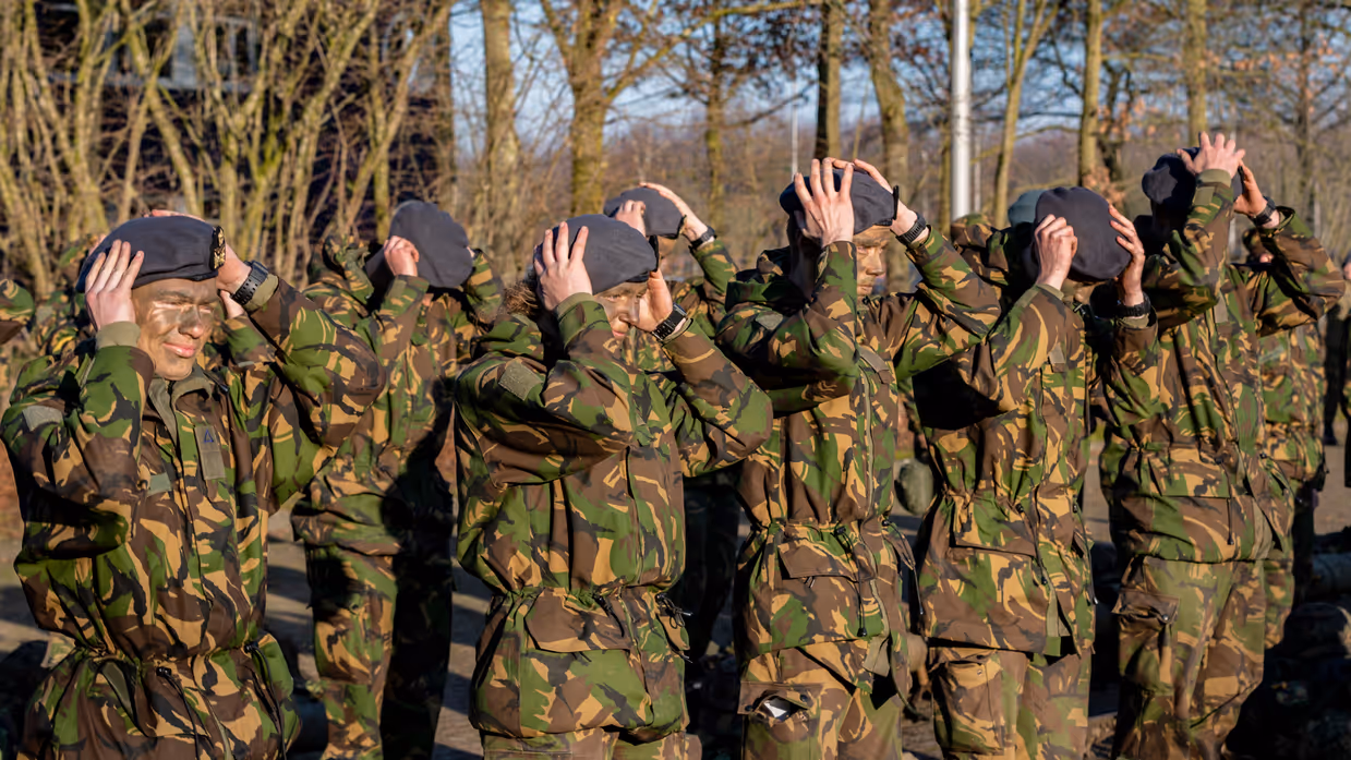 In rijen opgestelde militairen zetten hun baret op.