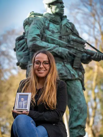 Vrouw zittend met een foto in de hand voor een bronzen beeld.