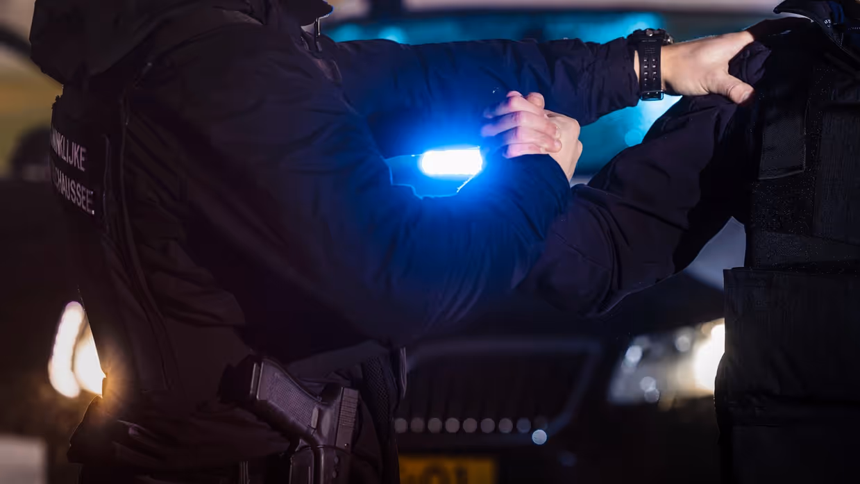 een marechaussee houdt met zijn handen een verdachte vast. 