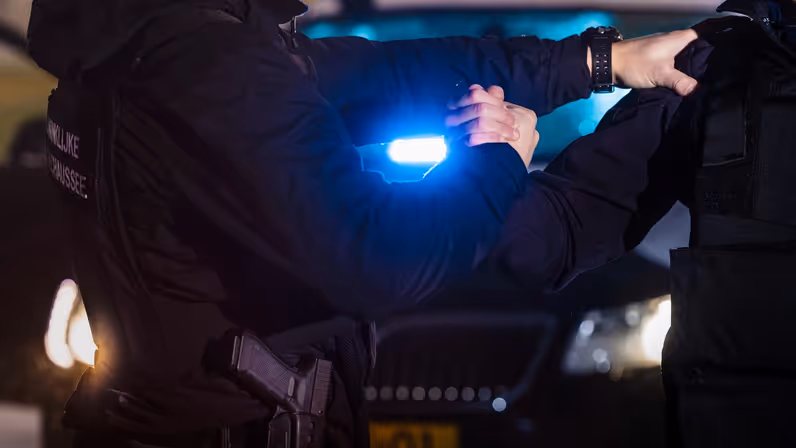 een marechaussee houdt met zijn handen een verdachte vast. 